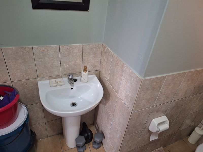 A compact bathroom featuring a white pedestal basin with a chrome mixer tap and neutral ceramic wall tiling.