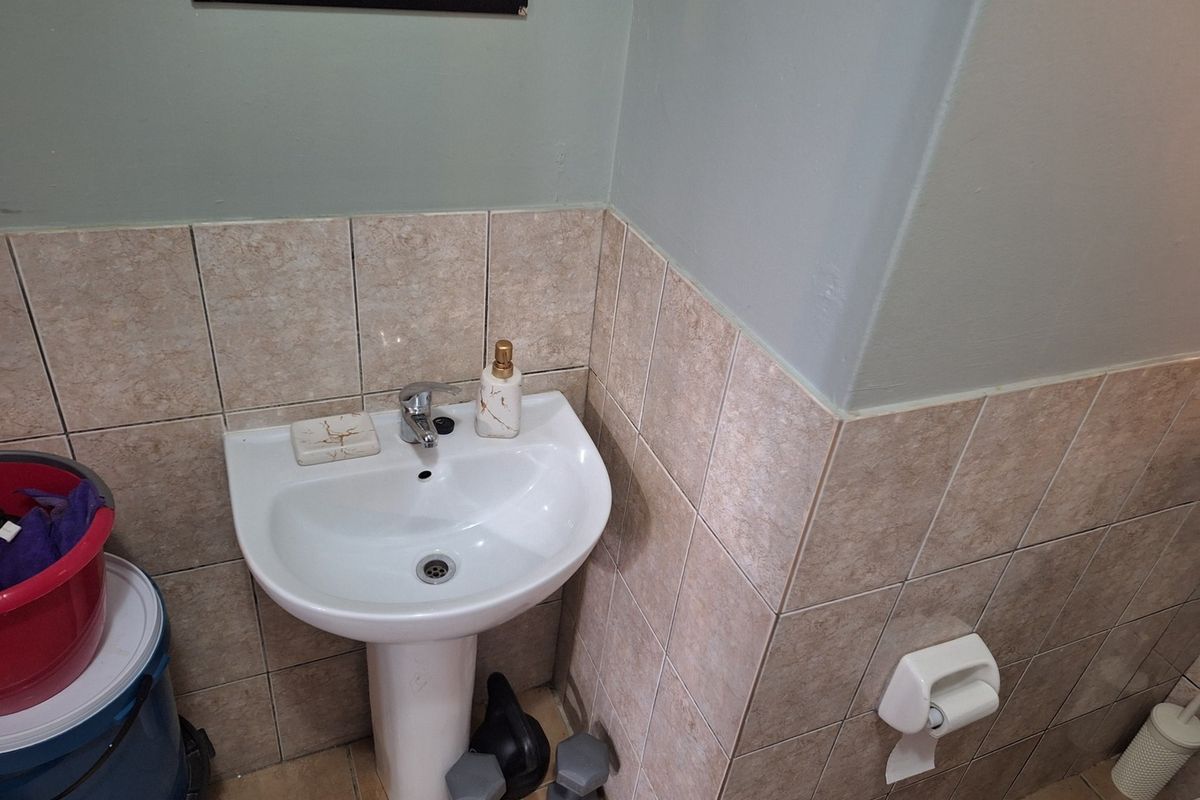A compact bathroom featuring a white pedestal basin with a chrome mixer tap and neutral ceramic wall tiling.