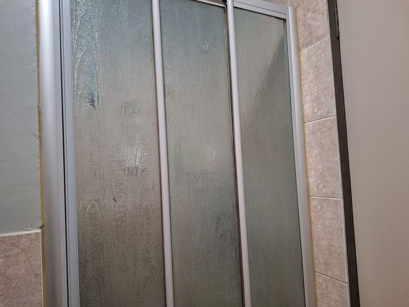 A close-up view of a bathroom shower enclosure featuring sliding glass doors and ceramic wall tiling, showing signs of wear and aging.