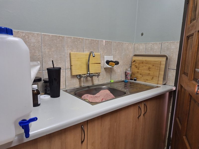 A functional kitchen area featuring a stainless steel sink, tiled backsplash, and wooden cabinetry with laminate countertops.