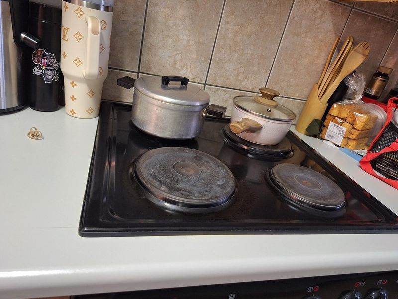 A close-up view of a kitchen workspace featuring a black electric hob and tiled splashback, showing signs of wear and daily use.