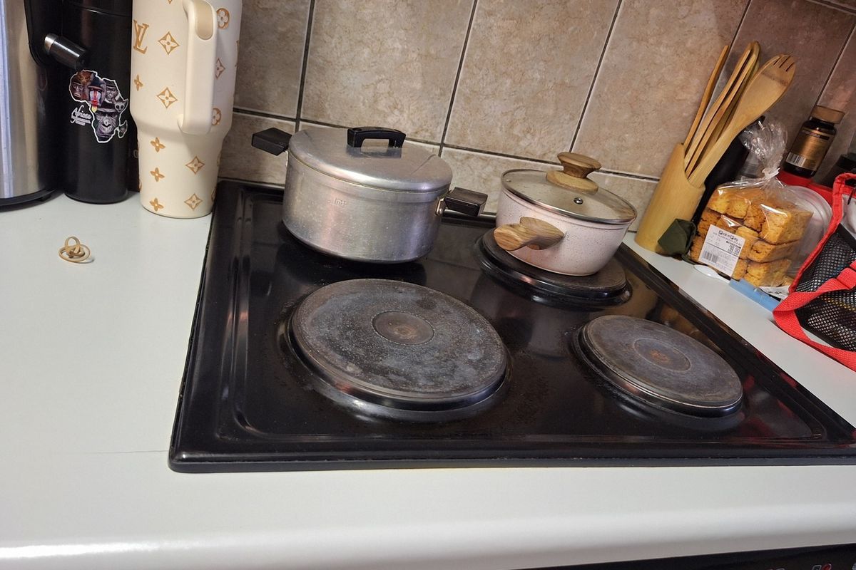 A close-up view of a kitchen workspace featuring a black electric hob and tiled splashback, showing signs of wear and daily use.