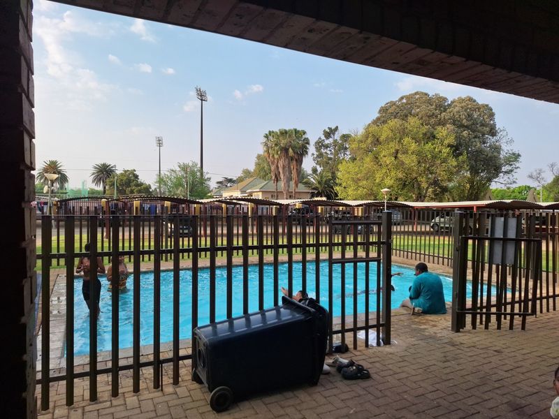 Outdoor swimming pool area featuring brick paving, metal security fencing, and a covered patio space.