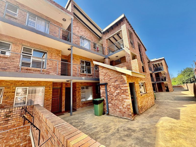 Exterior view of a multi-story apartment complex featuring face brick construction, metal balcony railings, and paved common areas.