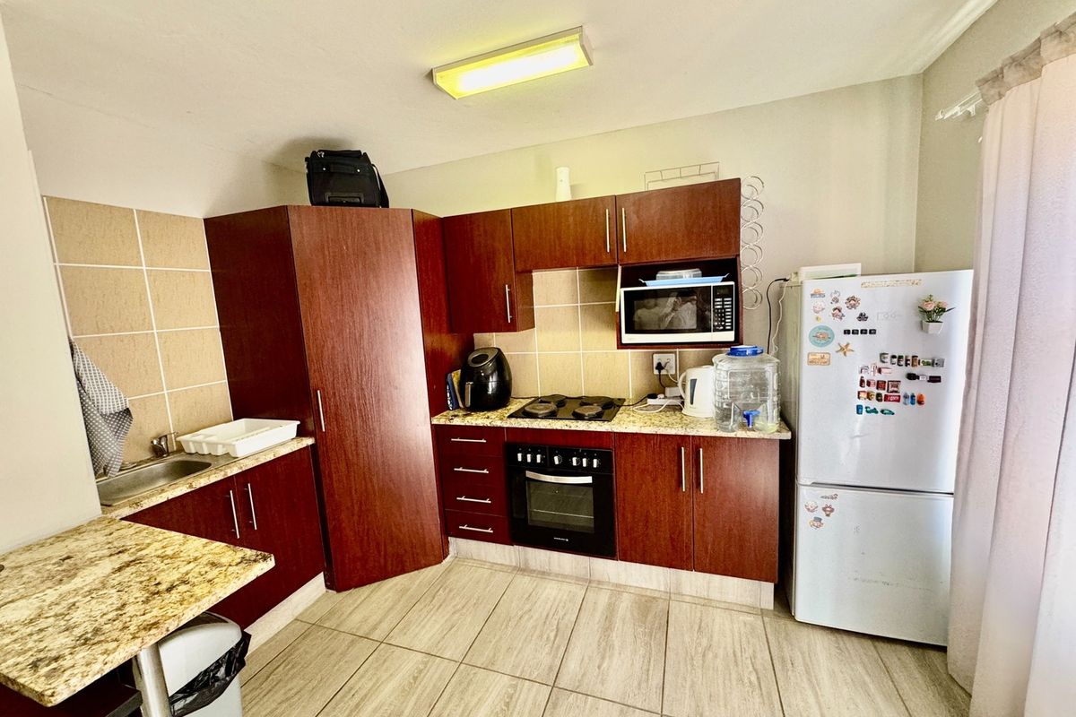 A functional kitchen featuring dark wood cabinetry, granite countertops, a built-in oven, gas hob, and tiled flooring.