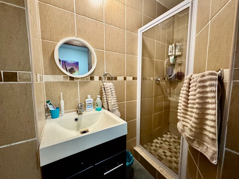Compact bathroom featuring a vanity cabinet with basin, tiled walls, and a separate shower enclosure with mosaic floor tiling.