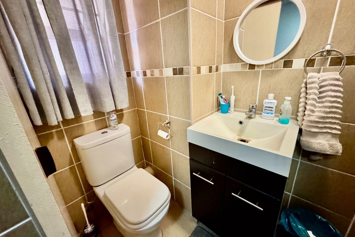 A compact bathroom featuring tiled walls and flooring, a modern vanity cabinet with a basin, and a standard toilet.