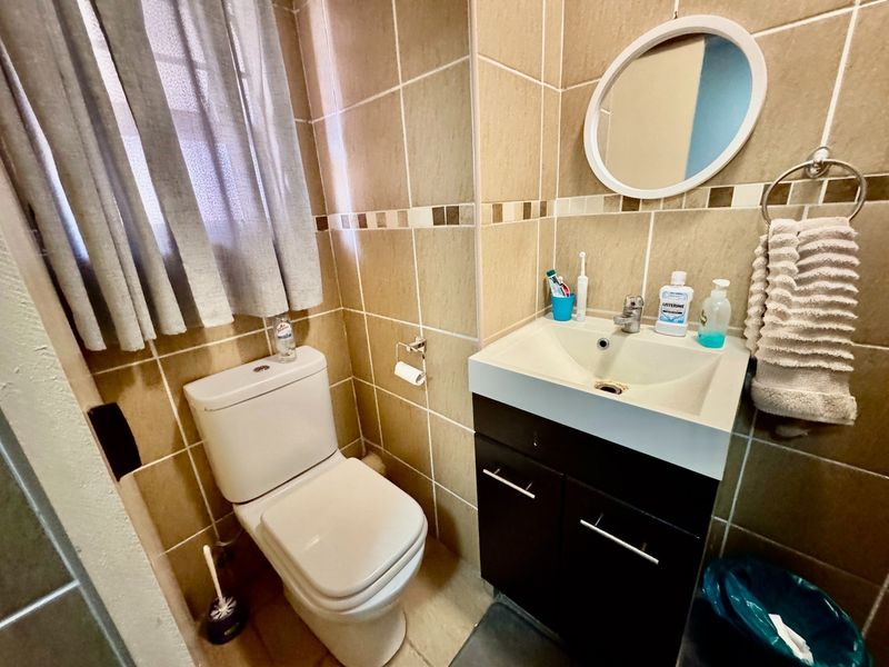 A compact bathroom featuring tiled walls and flooring, a modern vanity cabinet with a basin, and a standard toilet.