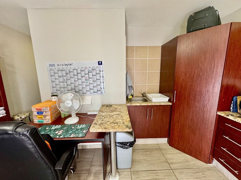 A functional scullery or utility area featuring built-in cabinetry, granite countertops, a stainless steel sink, and tiled finishes.