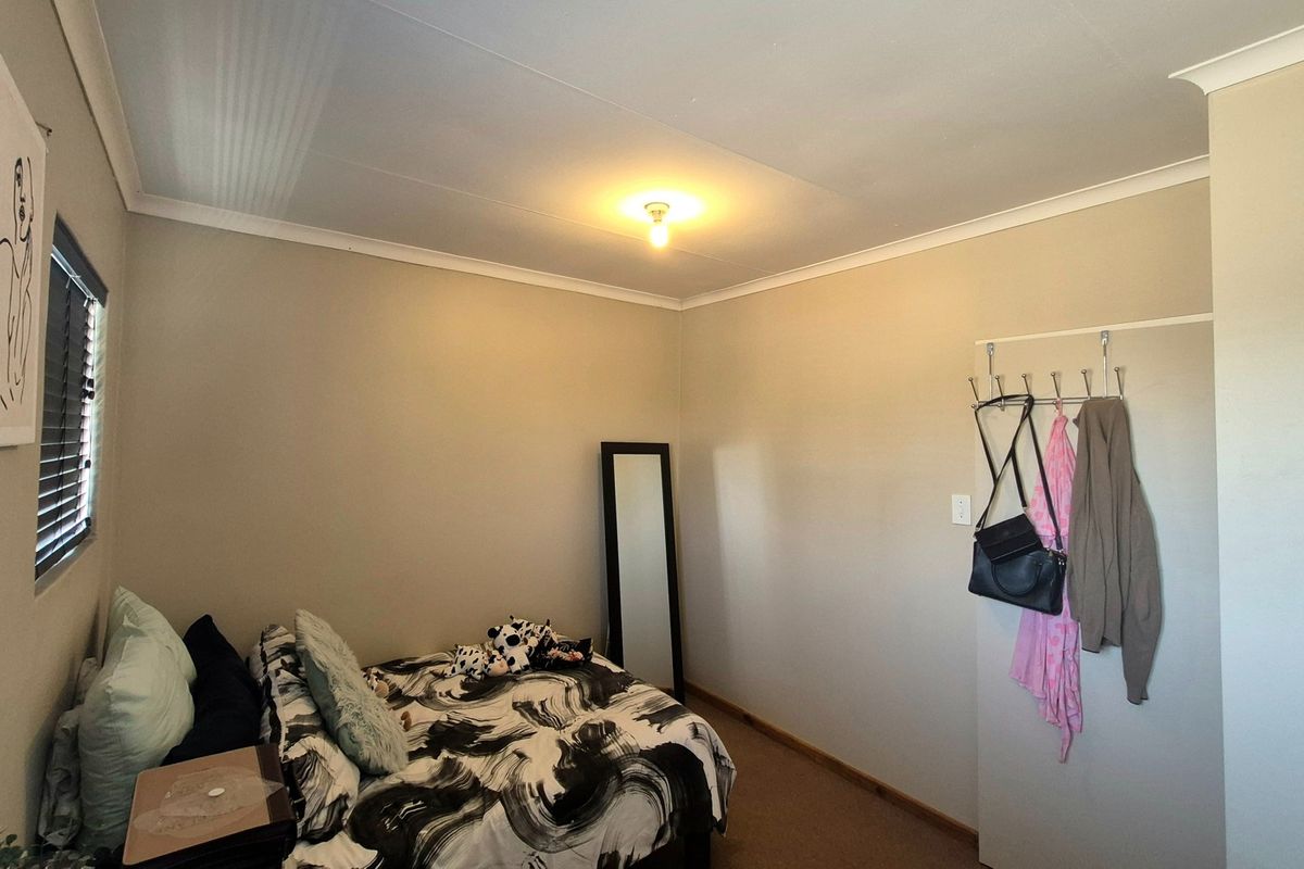 A functional bedroom featuring neutral wall tones, carpet flooring, and window blinds, providing a comfortable and well-lit living space.
