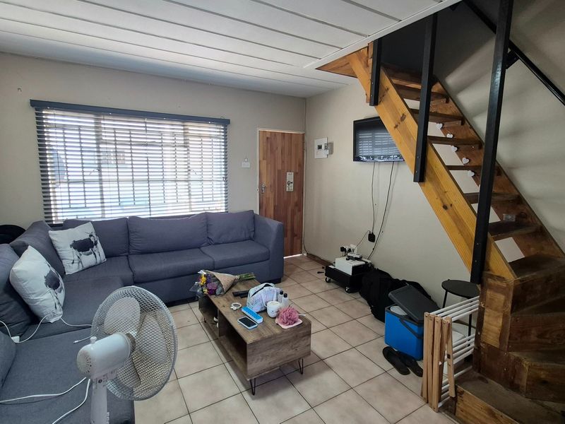 A living room featuring tiled flooring, venetian blinds, and a timber staircase leading to the upper level.