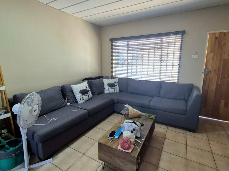 A functional living room featuring tiled flooring, a timber entrance door, and venetian blinds, providing a neutral base for interior updates.