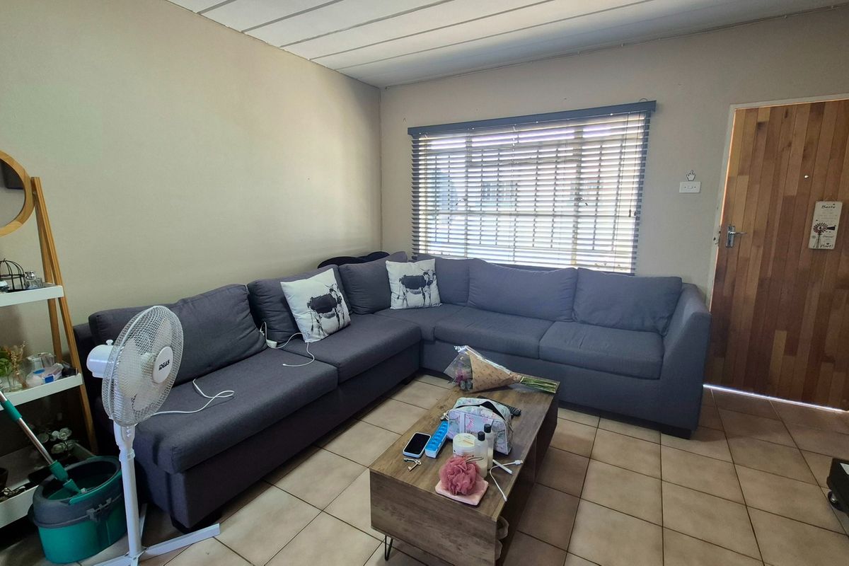 A functional living room featuring tiled flooring, a timber entrance door, and venetian blinds, providing a neutral base for interior updates.