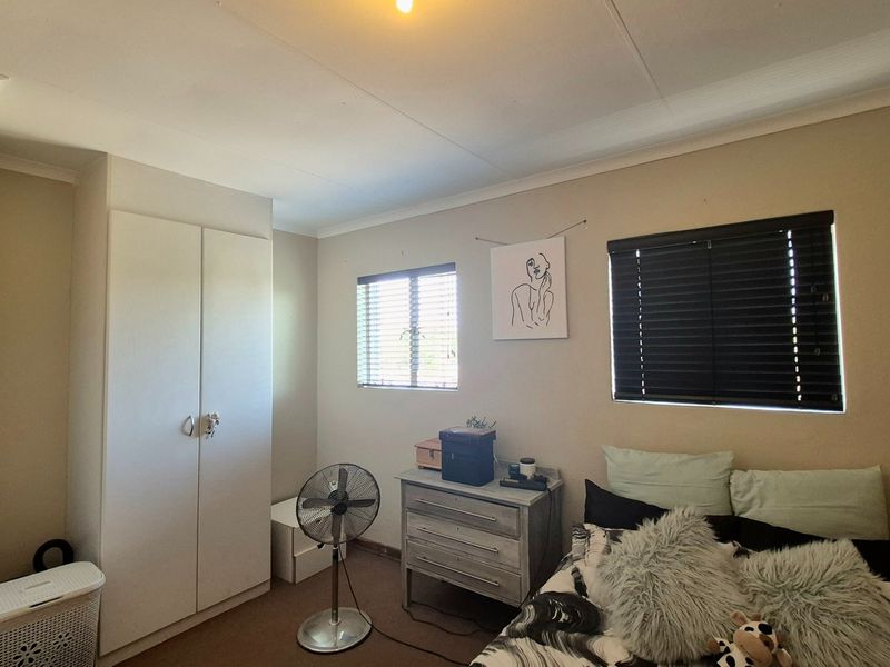 A functional bedroom featuring a built-in wardrobe, carpeted flooring, and dual windows fitted with venetian blinds for natural light control.