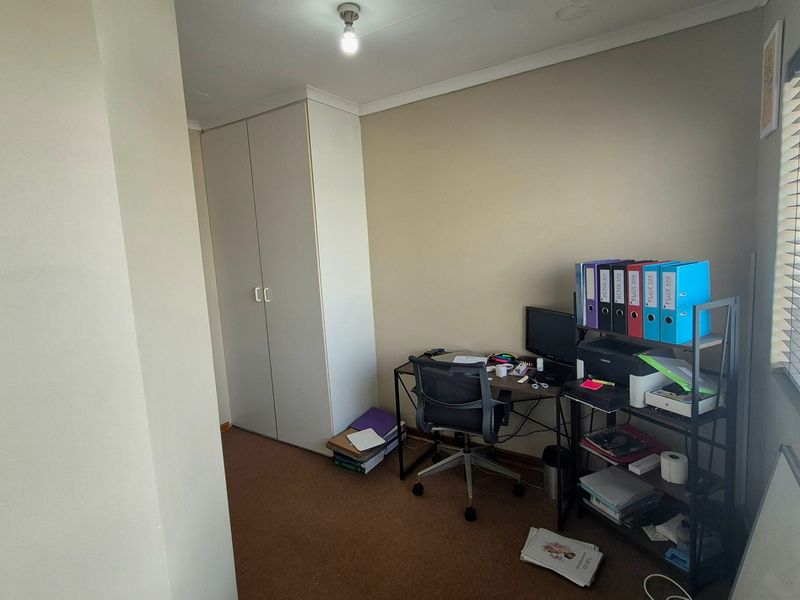 A compact bedroom featuring built-in wardrobe storage, carpeted flooring, and venetian blinds, currently utilized as a home office space.