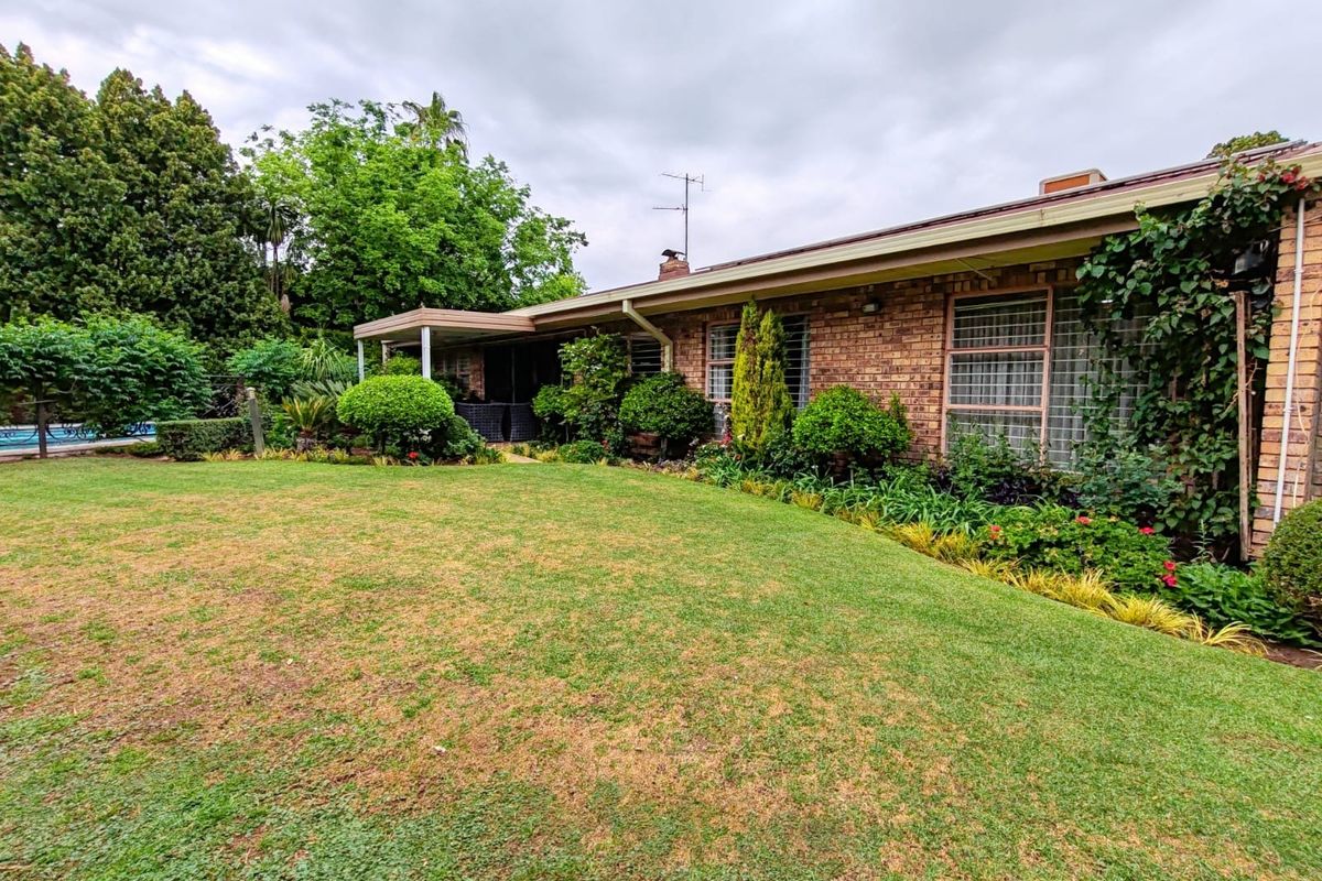 Rear view of a brick house featuring a covered patio area and an established garden with a lawn.