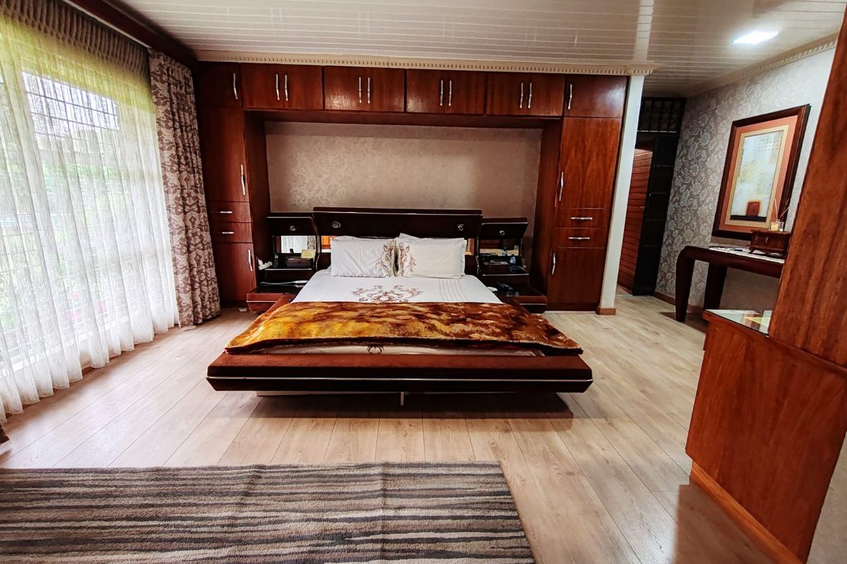 Spacious bedroom featuring extensive built-in wooden cabinetry, light-toned laminate flooring, and large windows with integrated curtains.