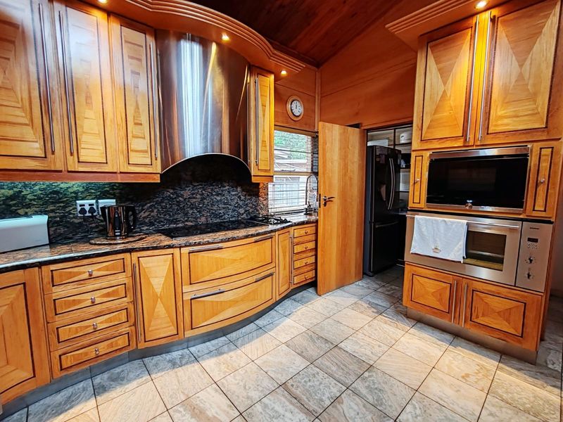 A well-appointed kitchen featuring custom wooden cabinetry, granite countertops, stainless steel built-in appliances, and tiled flooring under a warm wooden ceiling.