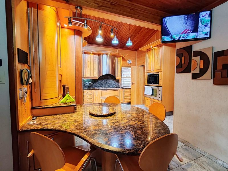A spacious kitchen featuring extensive wooden cabinetry, granite countertops, a built-in oven and microwave, and a distinctive timber-clad ceiling.