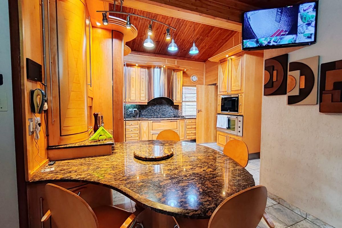 A spacious kitchen featuring extensive wooden cabinetry, granite countertops, a built-in oven and microwave, and a distinctive timber-clad ceiling.