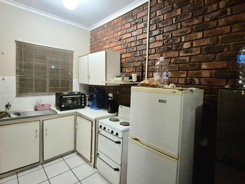 A compact kitchen featuring exposed brick walls, tiled flooring, built-in cabinetry, and a stainless steel sink with a freestanding stove.