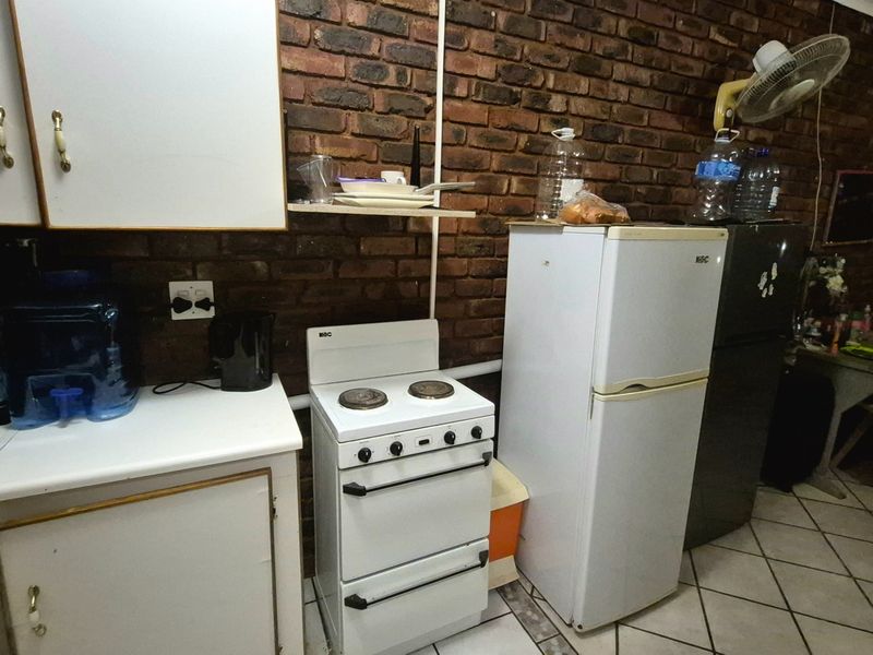 A functional kitchen featuring exposed brick walls, white cabinetry, laminate countertops, and a freestanding stove with ceramic tiled flooring.