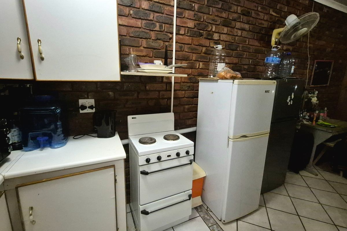 A functional kitchen featuring exposed brick walls, white cabinetry, laminate countertops, and a freestanding stove with ceramic tiled flooring.