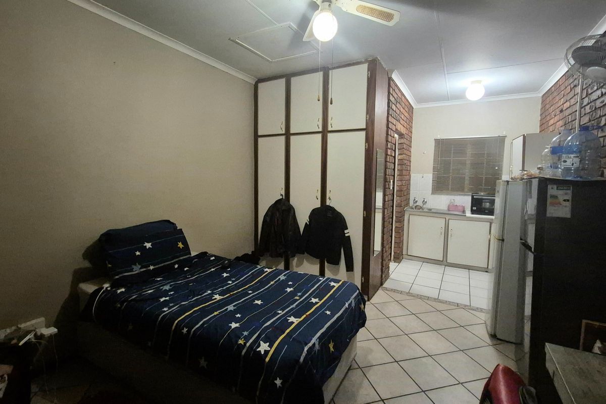 Open-plan studio apartment featuring a combined living and sleeping area with built-in cupboards and a compact kitchenette with tiled flooring.