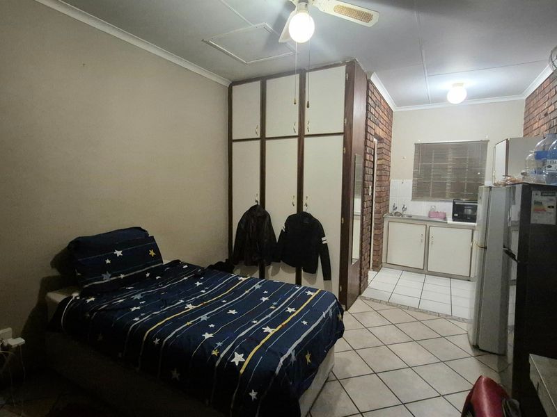 Open-plan studio apartment featuring a combined living and sleeping area with built-in cupboards and a compact kitchenette with tiled flooring.