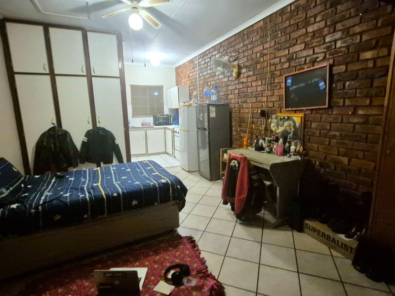 Open-plan studio apartment featuring an exposed brick wall, built-in cupboards, and a compact kitchen area with tiled flooring throughout.