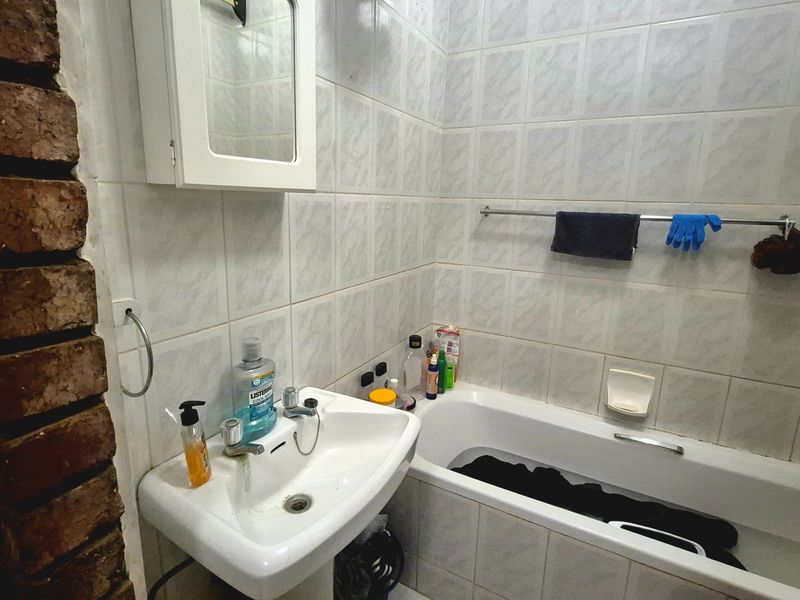 A compact bathroom featuring a pedestal basin, bathtub, and wall-mounted cabinet, accented by an exposed brick wall and tiled surfaces.