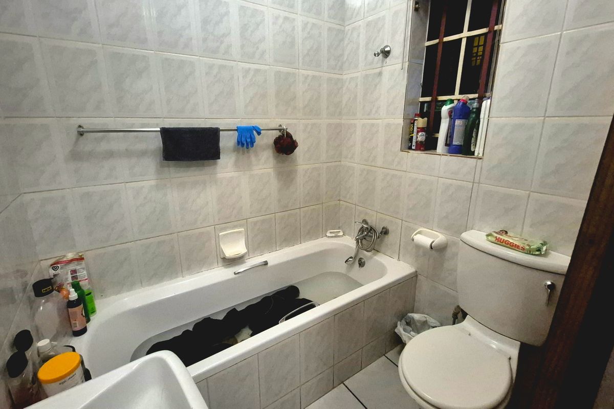 A functional bathroom featuring a standard bathtub, toilet, and full-height wall tiling, requiring cosmetic updates to improve its overall aesthetic appeal.