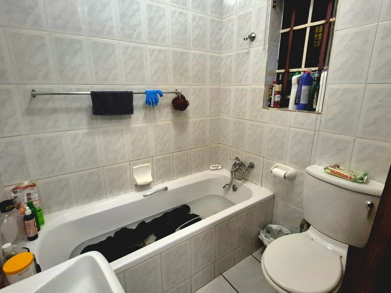 A functional bathroom featuring a standard bathtub, toilet, and full-height wall tiling, requiring cosmetic updates to improve its overall aesthetic appeal.