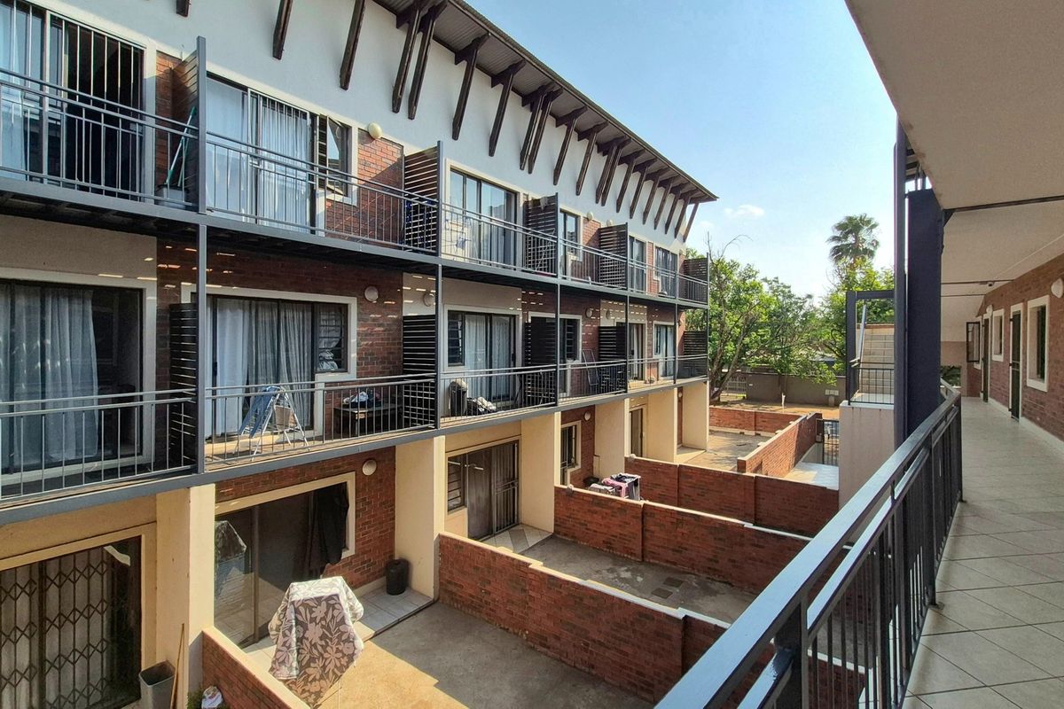 Exterior view of a multi-story apartment complex featuring brick facades, private balconies with metal railings, and ground-level courtyards with brick boundary walls.