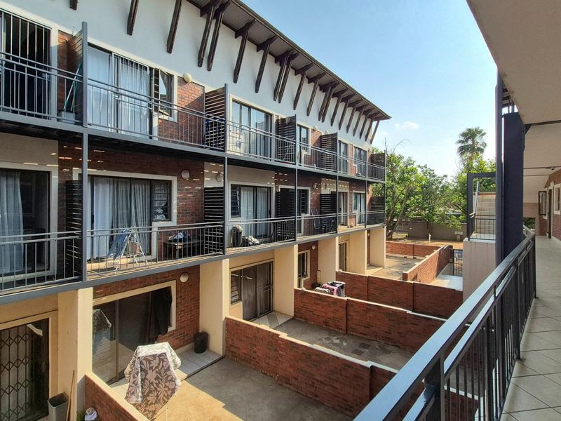 Exterior view of a multi-story apartment complex featuring brick facades, private balconies with metal railings, and ground-level courtyards with brick boundary walls.