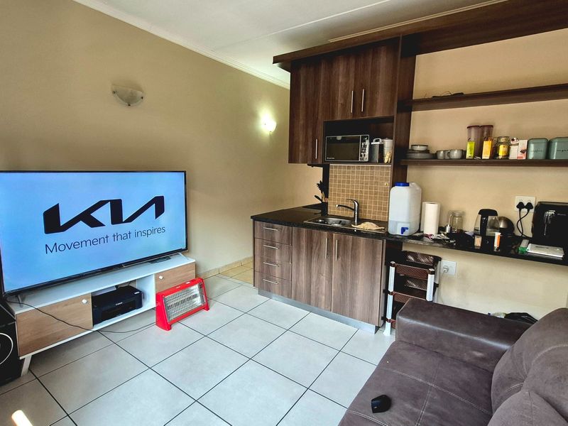 Compact open-plan living area featuring a kitchenette with dark wood cabinetry, tiled flooring, and integrated shelving.