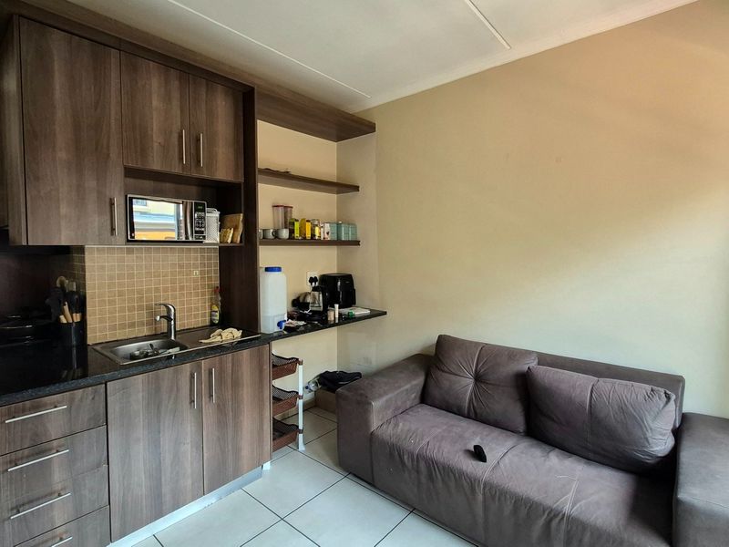 Compact open-plan kitchen and living area featuring modern wood-finish cabinetry, dark countertops, and tiled flooring, providing a functional space for daily living.