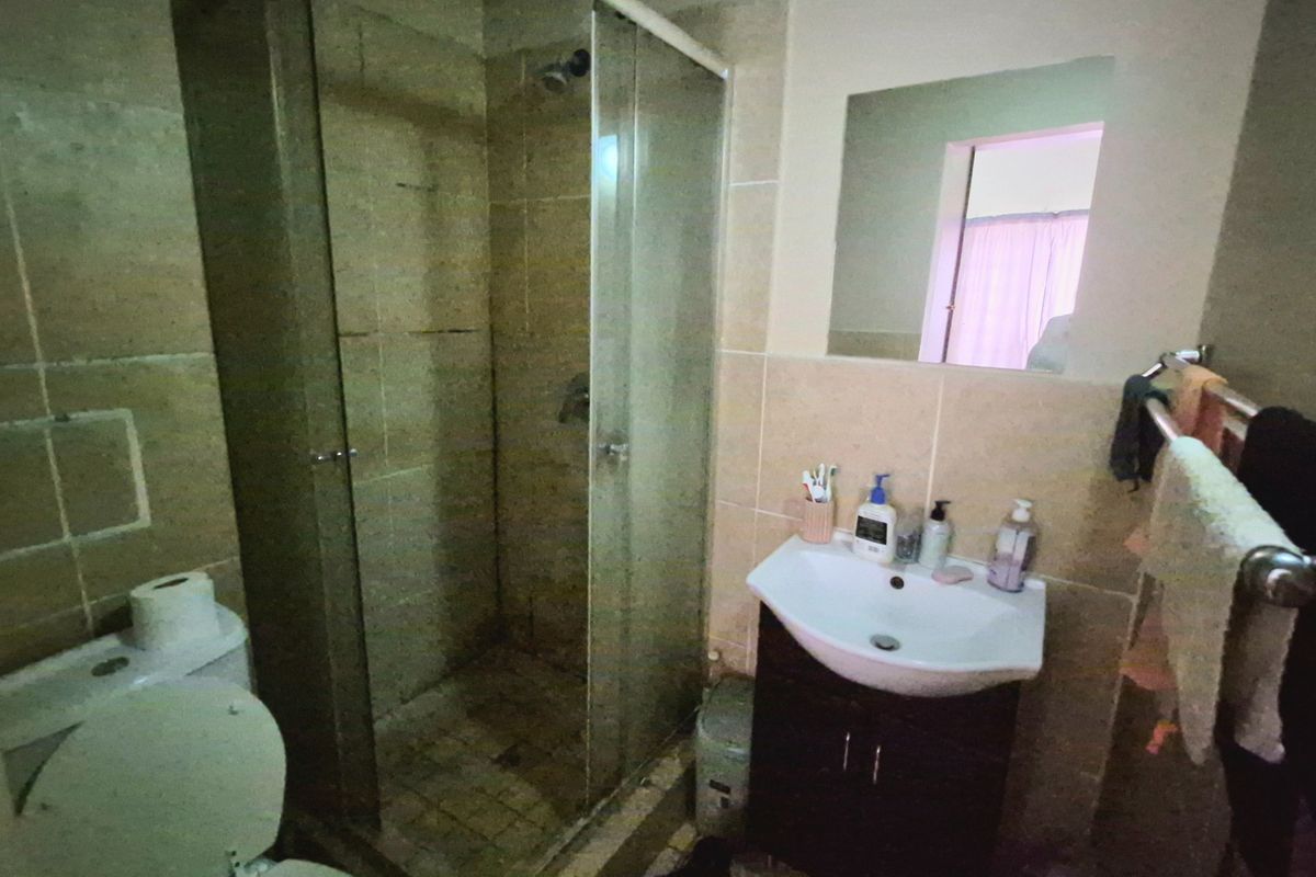 A functional bathroom featuring a shower enclosure, vanity cabinet with basin, wall mirror, and tiled finishes throughout.