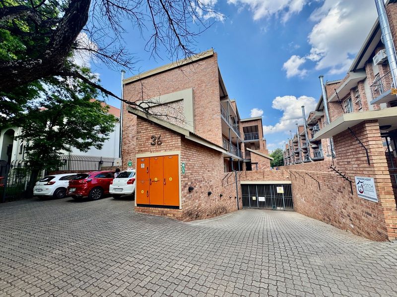 Exterior view of the apartment complex entrance featuring a brick facade, paved driveway, and secure underground parking access.