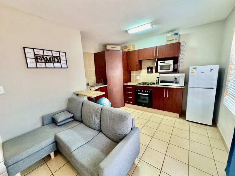 Open-plan kitchen and living area featuring dark wood cabinetry, granite countertops, built-in oven, hob, and tiled flooring throughout.