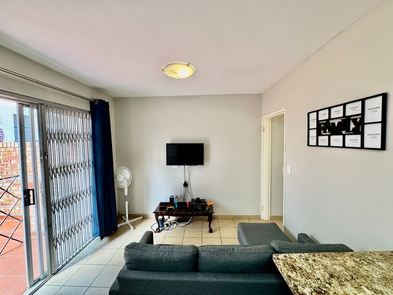 A living room featuring tiled flooring, a ceiling light fixture, and a sliding glass door with a security gate leading to an outdoor area.
