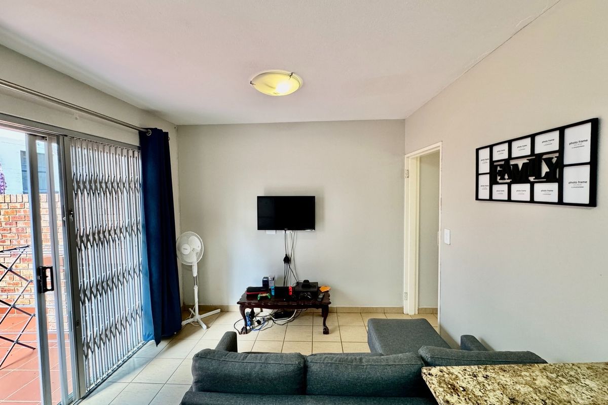 A living room featuring tiled flooring, a ceiling light fixture, and a sliding glass door with a security gate leading to an outdoor area.