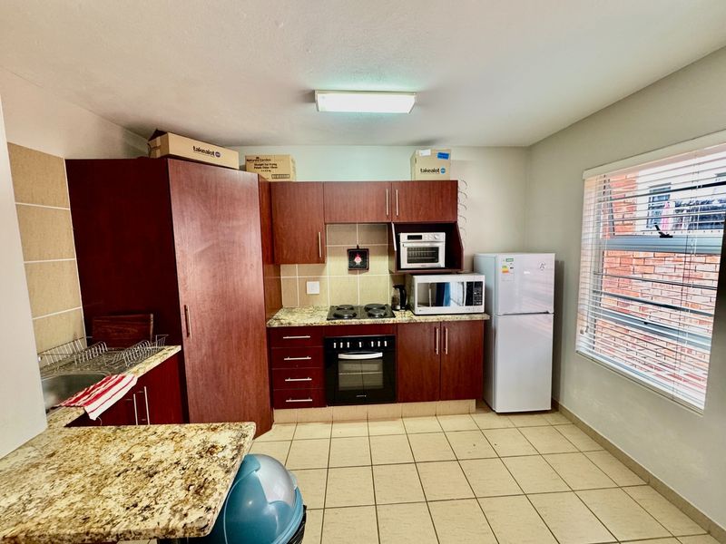 A functional kitchen featuring dark wood cabinetry, granite countertops, built-in oven and hob, and tiled flooring with a window providing natural light.