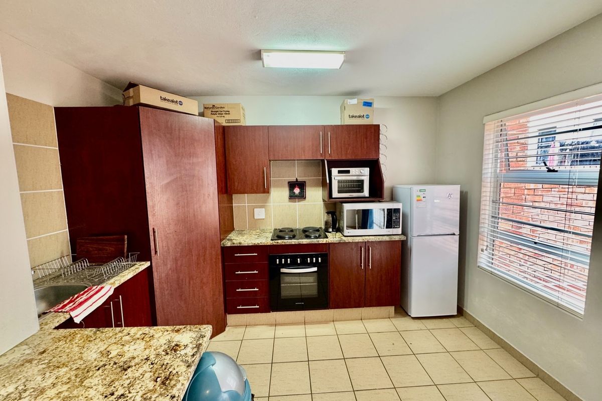 A functional kitchen featuring dark wood cabinetry, granite countertops, built-in oven and hob, and tiled flooring with a window providing natural light.