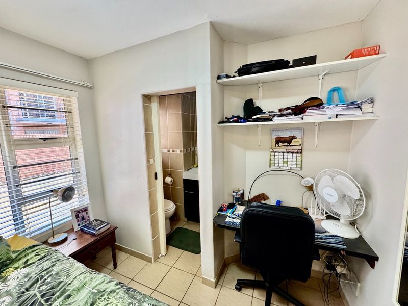 A functional bedroom featuring tiled flooring, built-in desk workspace with shelving, and direct access to an en-suite bathroom.
