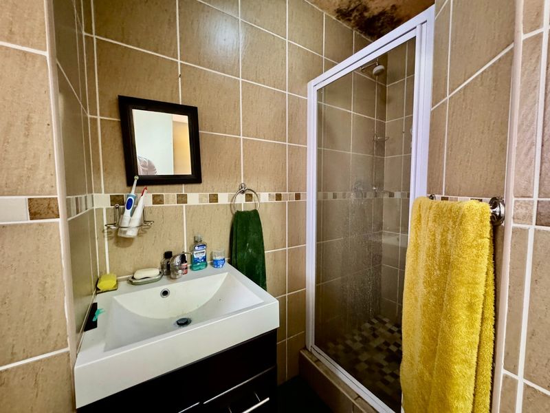 Compact bathroom featuring a vanity basin and a glass-enclosed shower, with tiled finishes throughout. Note visible ceiling water damage requiring attention.