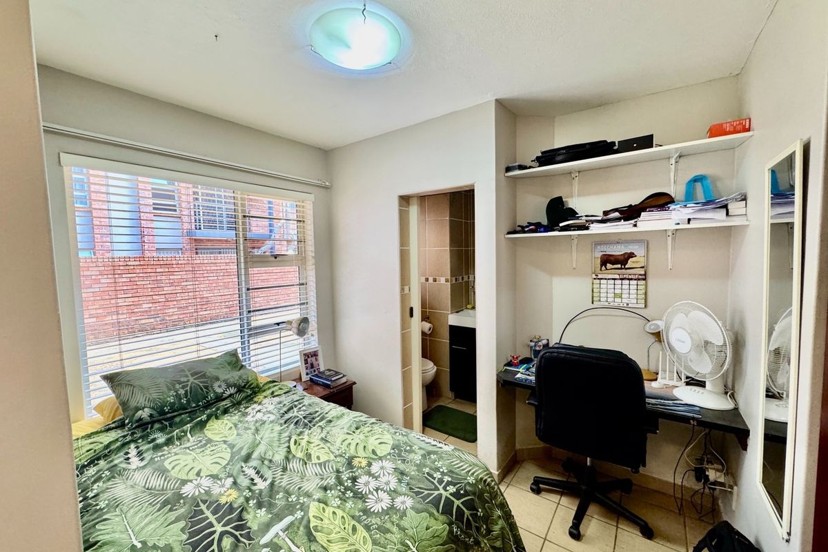 A functional bedroom featuring tiled flooring, built-in shelving, and direct access to an en-suite bathroom, with natural light provided by a large window.