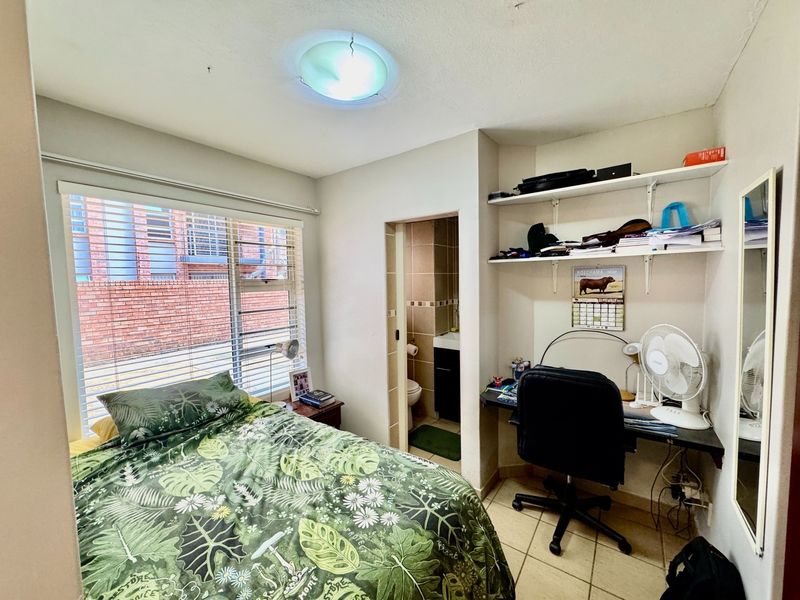 A functional bedroom featuring tiled flooring, built-in shelving, and direct access to an en-suite bathroom, with natural light provided by a large window.