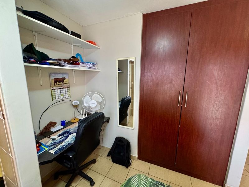 A functional bedroom featuring a large built-in wooden wardrobe, wall-mounted shelving units, and durable tiled flooring.