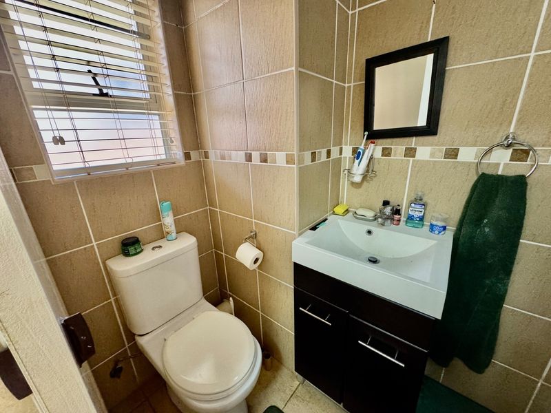 Compact bathroom featuring tiled walls, a modern vanity cabinet with basin, and a standard toilet, complemented by a window with venetian blinds.